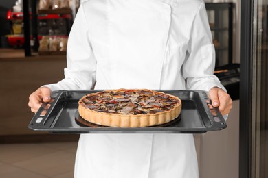 Photo of Baker holding delicious quiche at door of her cafe, closeup