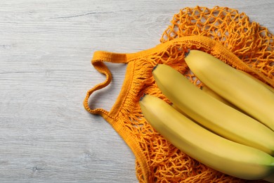 Photo of Net bag with bananas on white wooden table, top view. Space for text