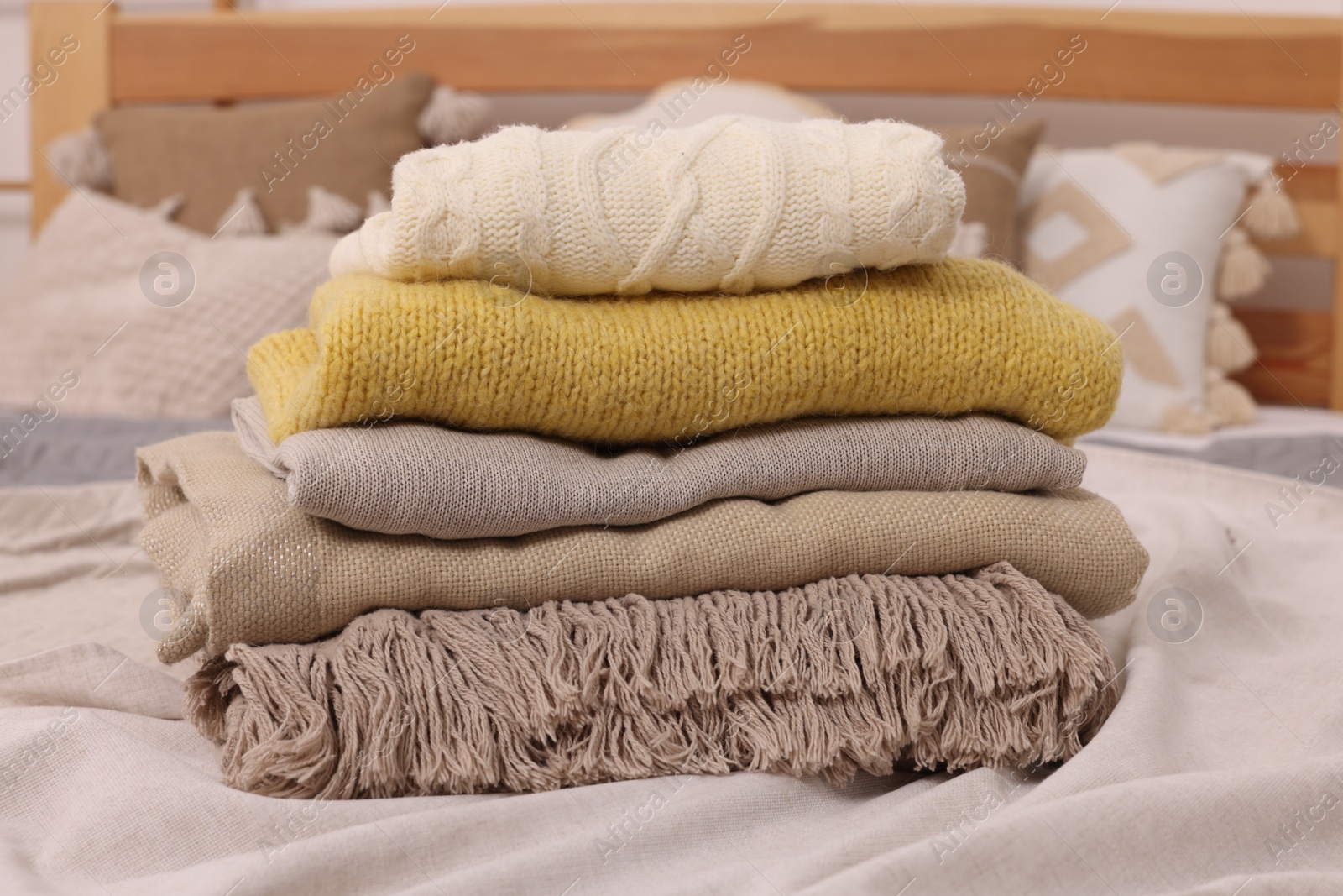 Photo of Stack of different folded blankets and clothes on bed. Home textile