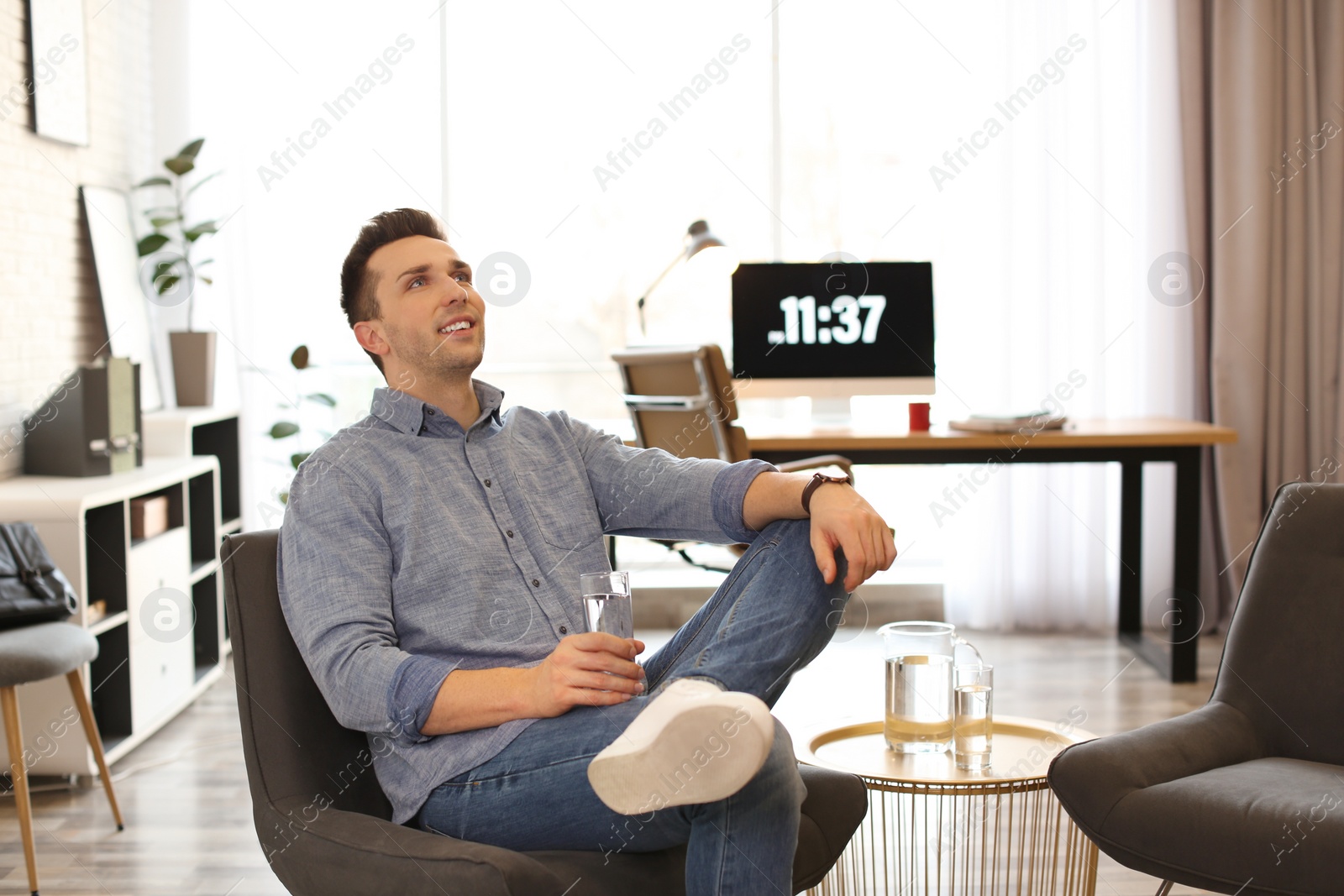 Photo of Young man with glass of water relaxing in comfortable chair at workplace