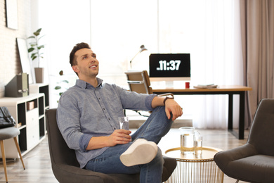 Photo of Young man with glass of water relaxing in comfortable chair at workplace