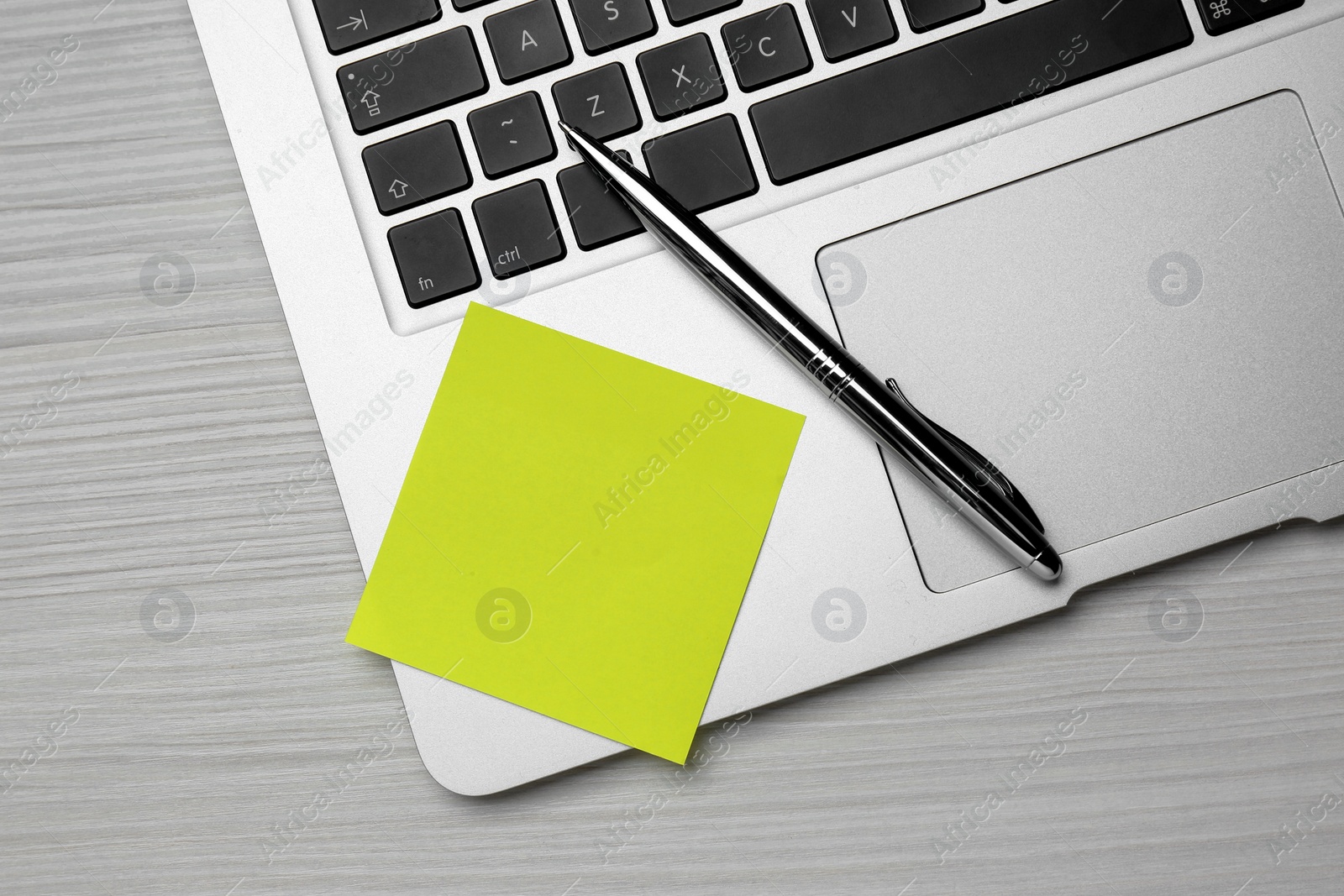 Photo of Laptop with blank sticky note and pen on white wooden table, top view. Space for text