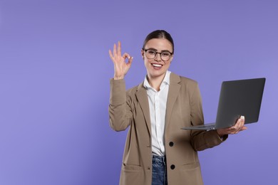 Photo of Happy woman in glasses with laptop showing okay gesture on violet background. Space for text