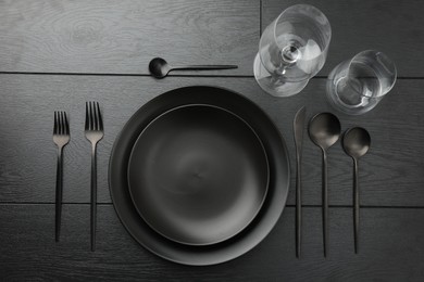 Stylish setting with cutlery and plates on black wooden table, flat lay