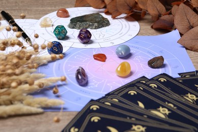 Photo of Zodiac wheel, tarot cards, astrology dices and gemstones on wooden table, closeup