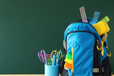 Photo of Stylish backpack and different school stationery near green chalkboard, space for text. Back to school
