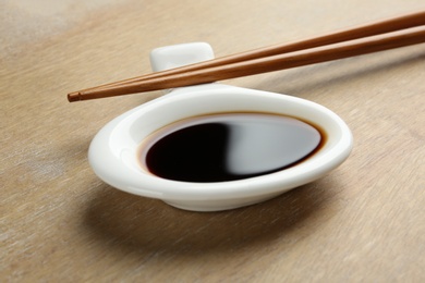 Dish of soy sauce with chopsticks on wooden background, closeup