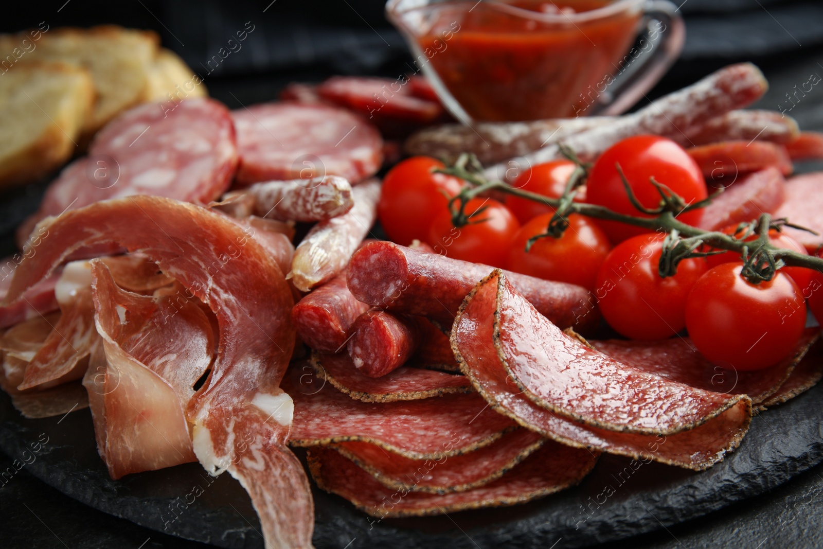 Photo of Different types of sausages with tomatoes served on slate board, closeup
