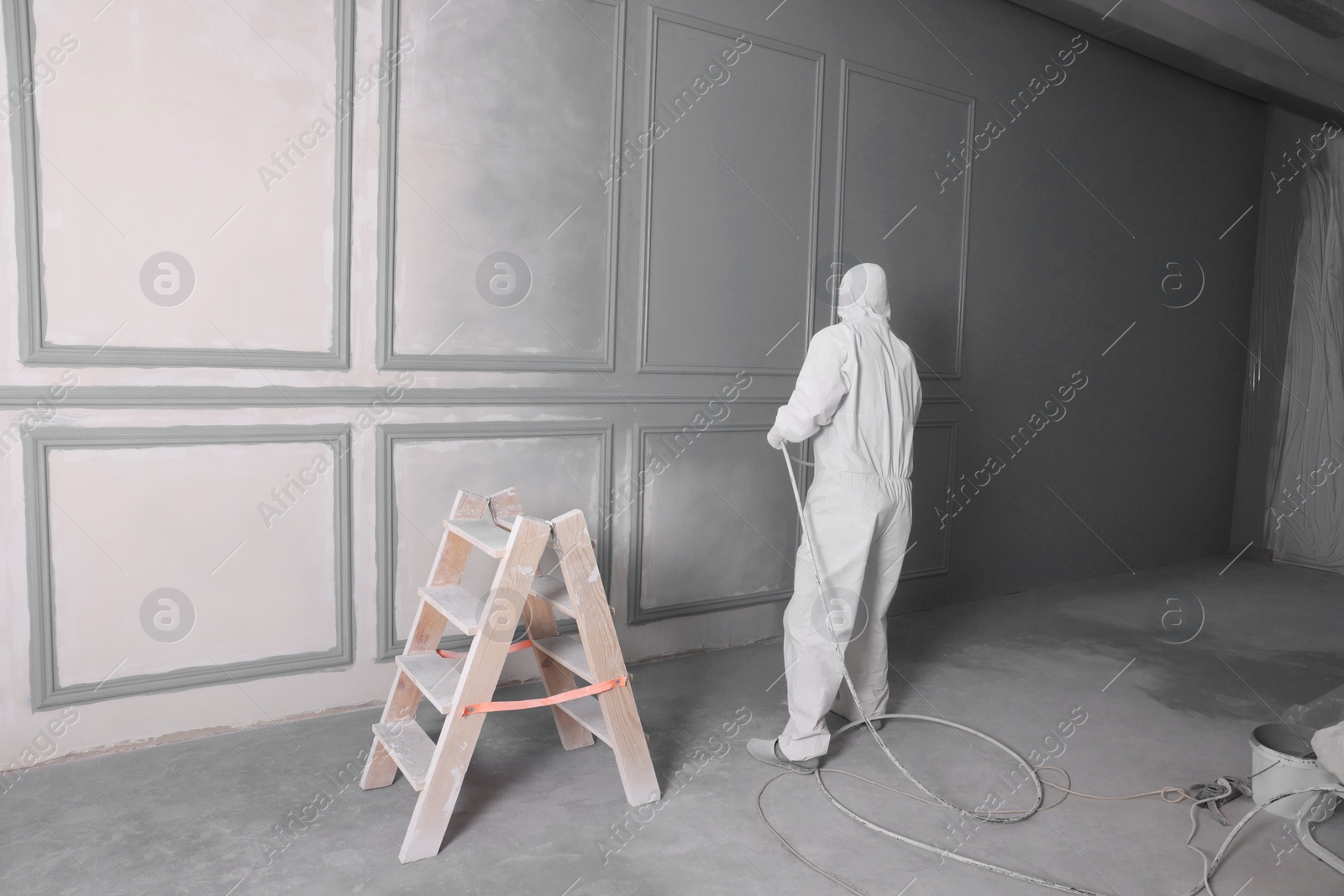 Photo of Decorator dyeing wall in grey color with spray paint indoors, back view