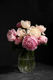 Photo of Bouquet of beautiful peonies in glass vase on dark table against black background