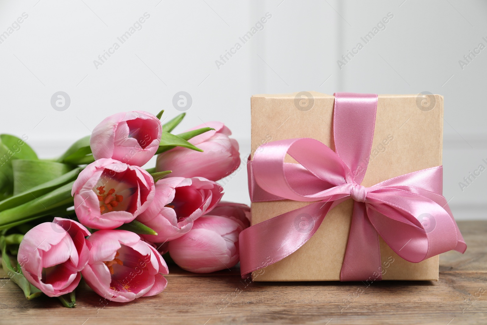 Photo of Beautiful gift box with bow and pink tulips on wooden table, closeup