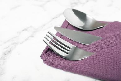 Folded napkin with fork, spoon and knife on marble background, closeup