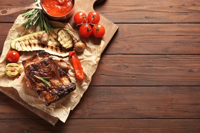 Photo of Flat lay composition with delicious barbecued meat on wooden background. Space for text