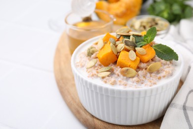 Photo of Tasty wheat porridge with pumpkin and mint in bowl on white table, closeup. Space for text