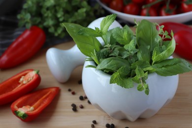 Photo of Mortar with different fresh herbs and pepper on wooden table, closeup