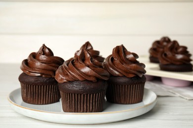 Photo of Plate with delicious chocolate cupcakes on white wooden table