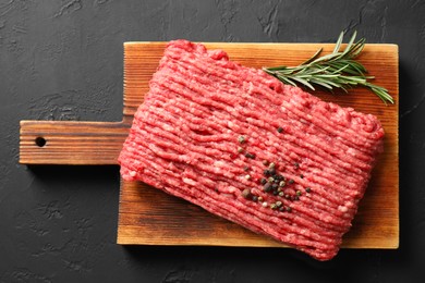 Photo of Raw ground meat, rosemary and peppercorns on black table, top view