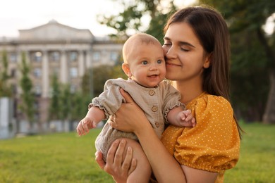 Happy mother with adorable baby walking in park on sunny day, space for text