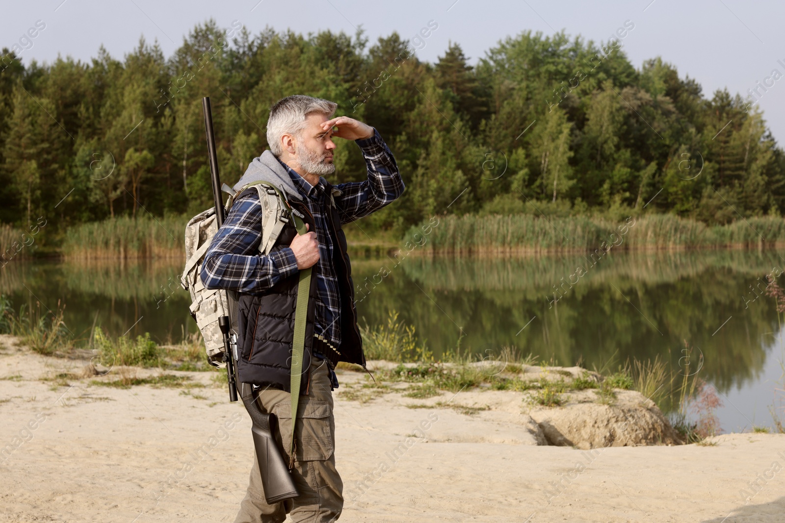 Photo of Man with hunting rifle near lake outdoors. Space for text