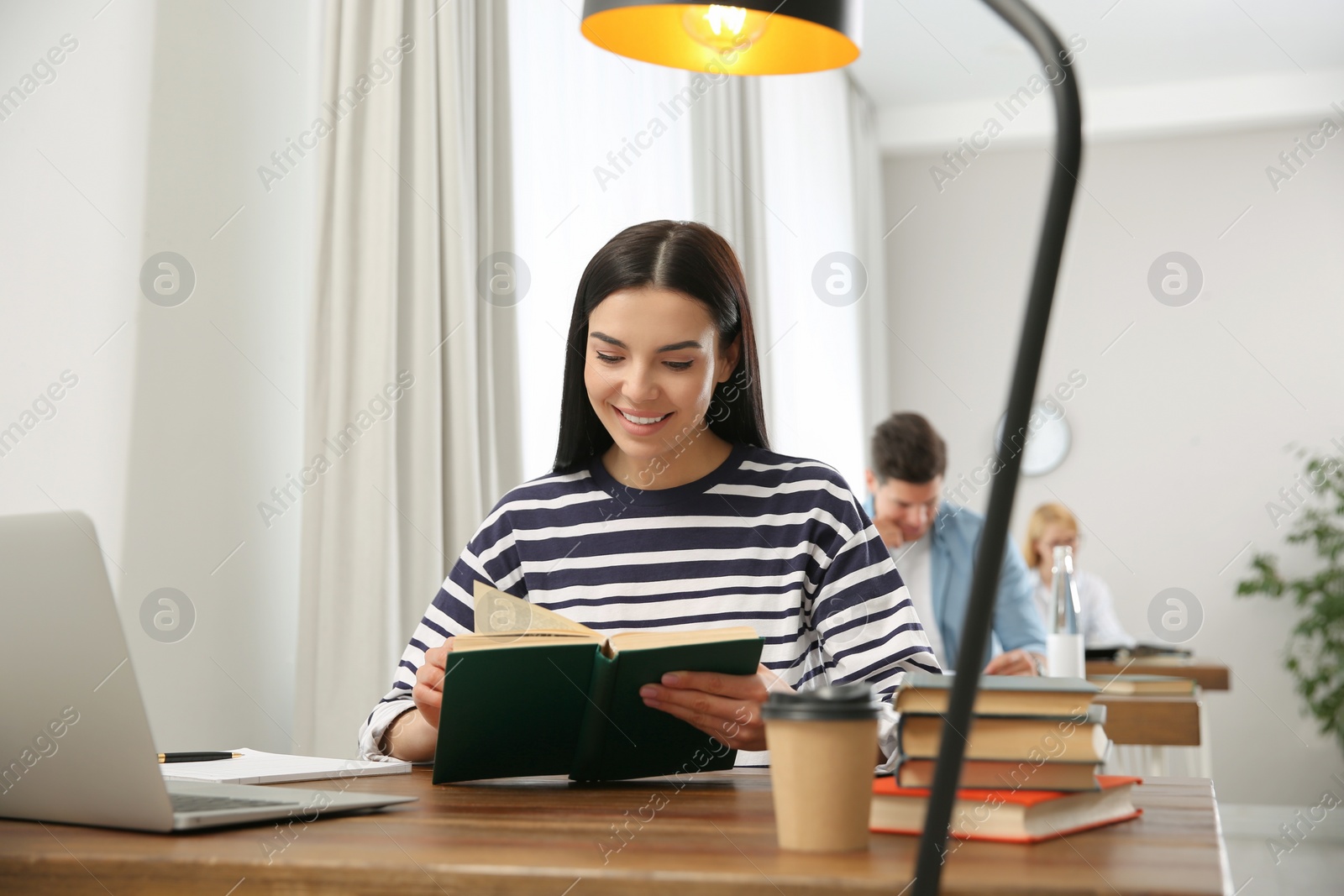 Photo of Young woman reading book at table in library