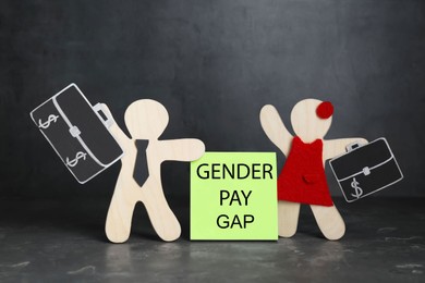 Photo of Gender pay gap. Wooden figures of man and woman on black table