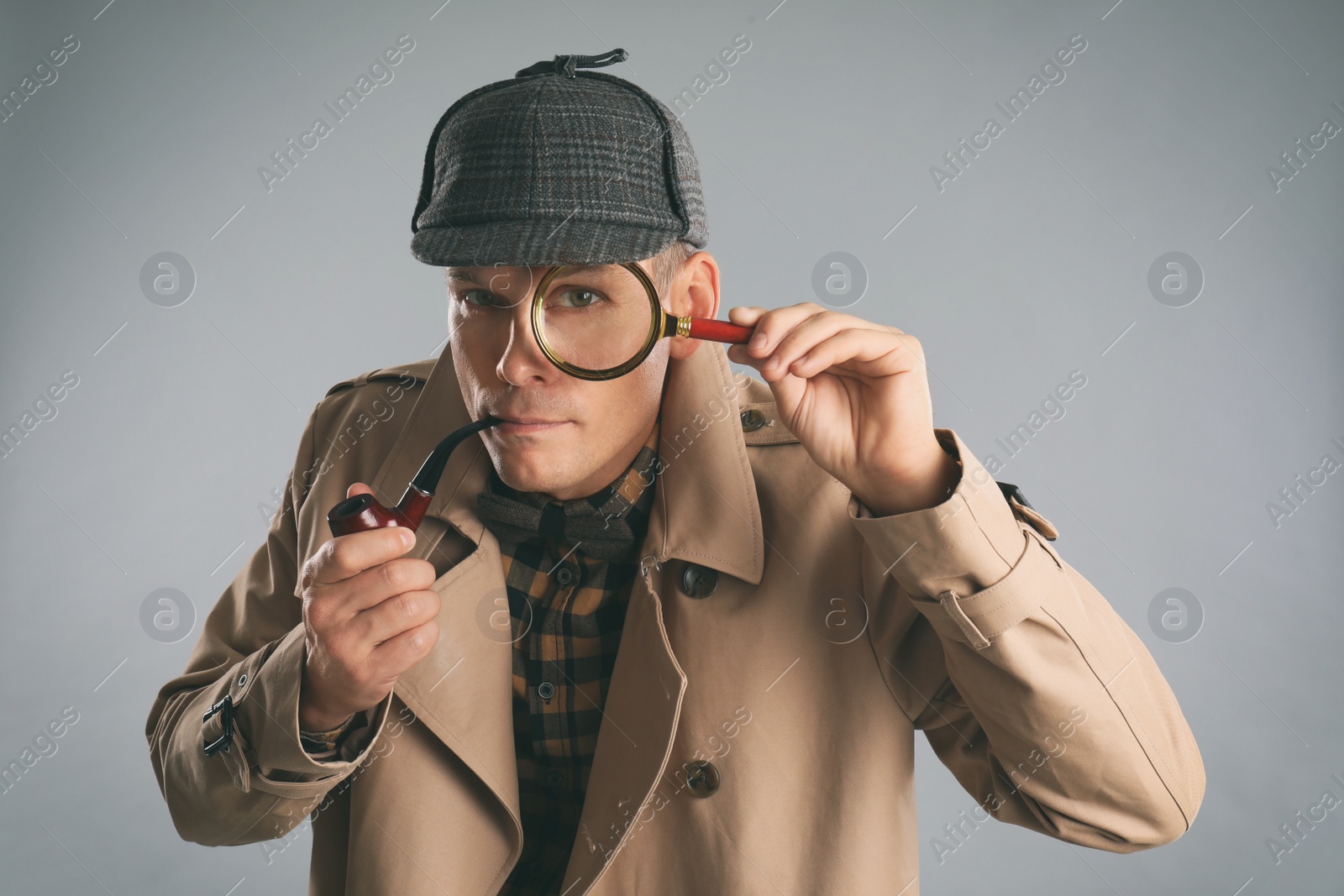 Photo of Male detective with magnifying glass smoking pipe on grey background