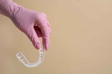 Photo of Bite correction. Dentist in medical glove holding mouth guard on beige background, closeup. Space for text