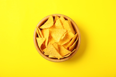Photo of Tasty mexican nachos chips in wooden bowl on yellow background, top view