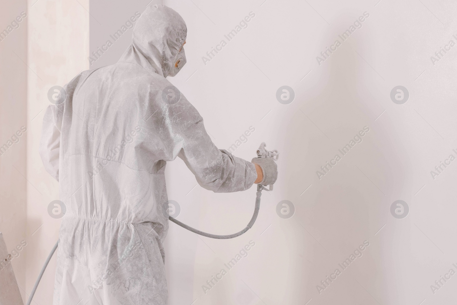 Photo of Decorator in uniform painting wall with sprayer indoors