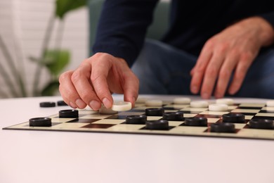 Man playing checkers at white table indoors, closeup