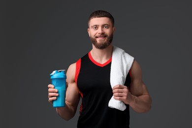 Young man with muscular body holding shaker of protein and towel on grey background