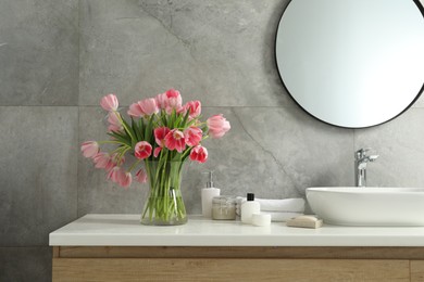 Vase with beautiful pink tulips and toiletries near sink in bathroom