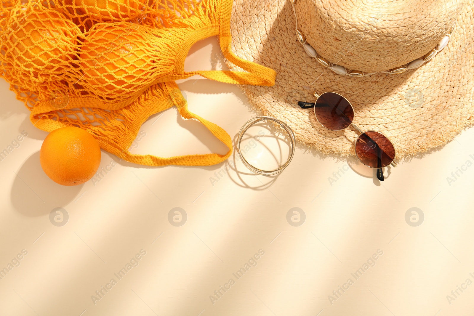 Photo of String bag with sunglasses, oranges and summer accessories on beige background, flat lay. Space for text