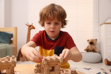 Photo of Little boy playing with wooden construction set at table in room. Child's toy