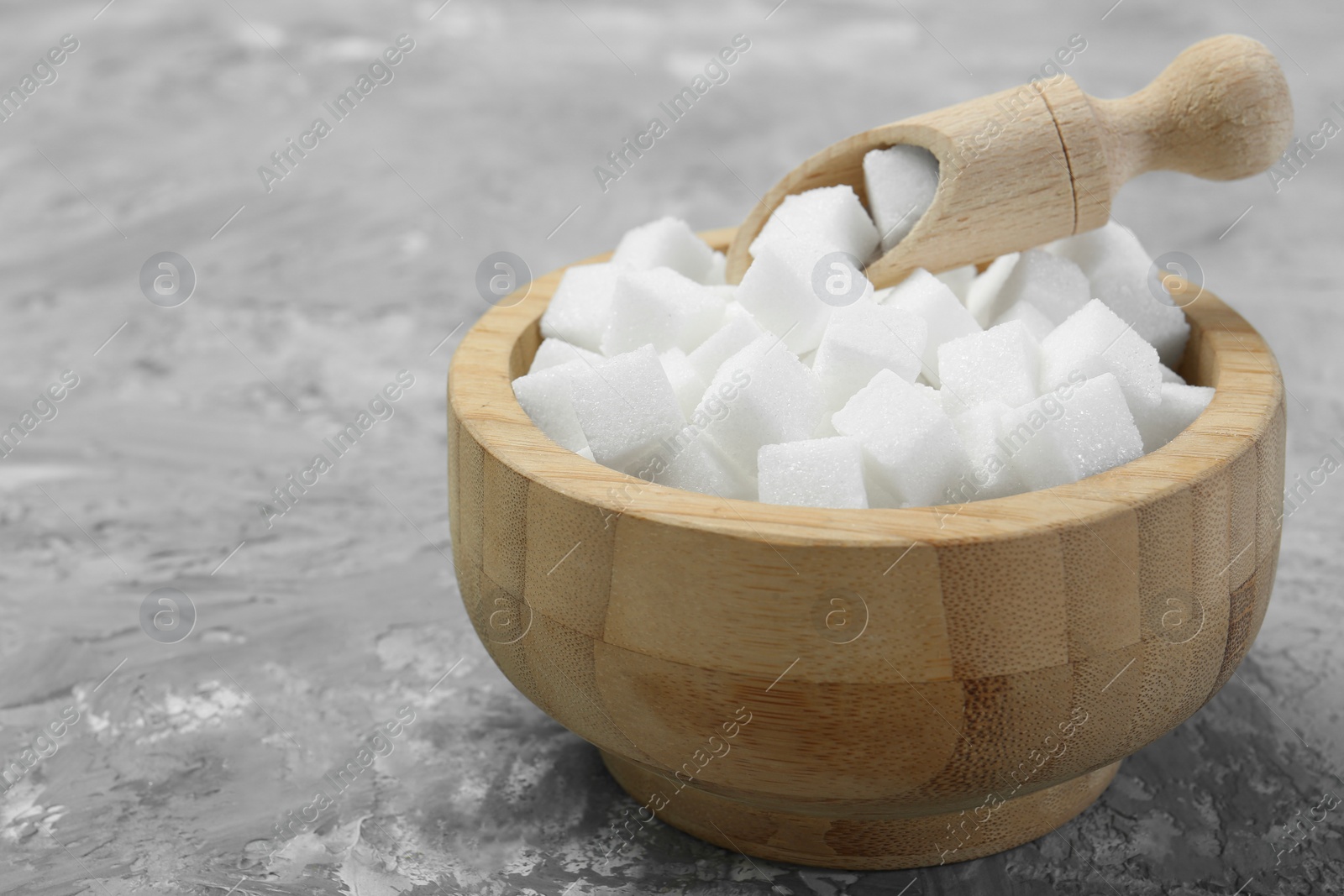 Photo of White sugar cubes in wooden bowl and scoop on grey table. Space for text