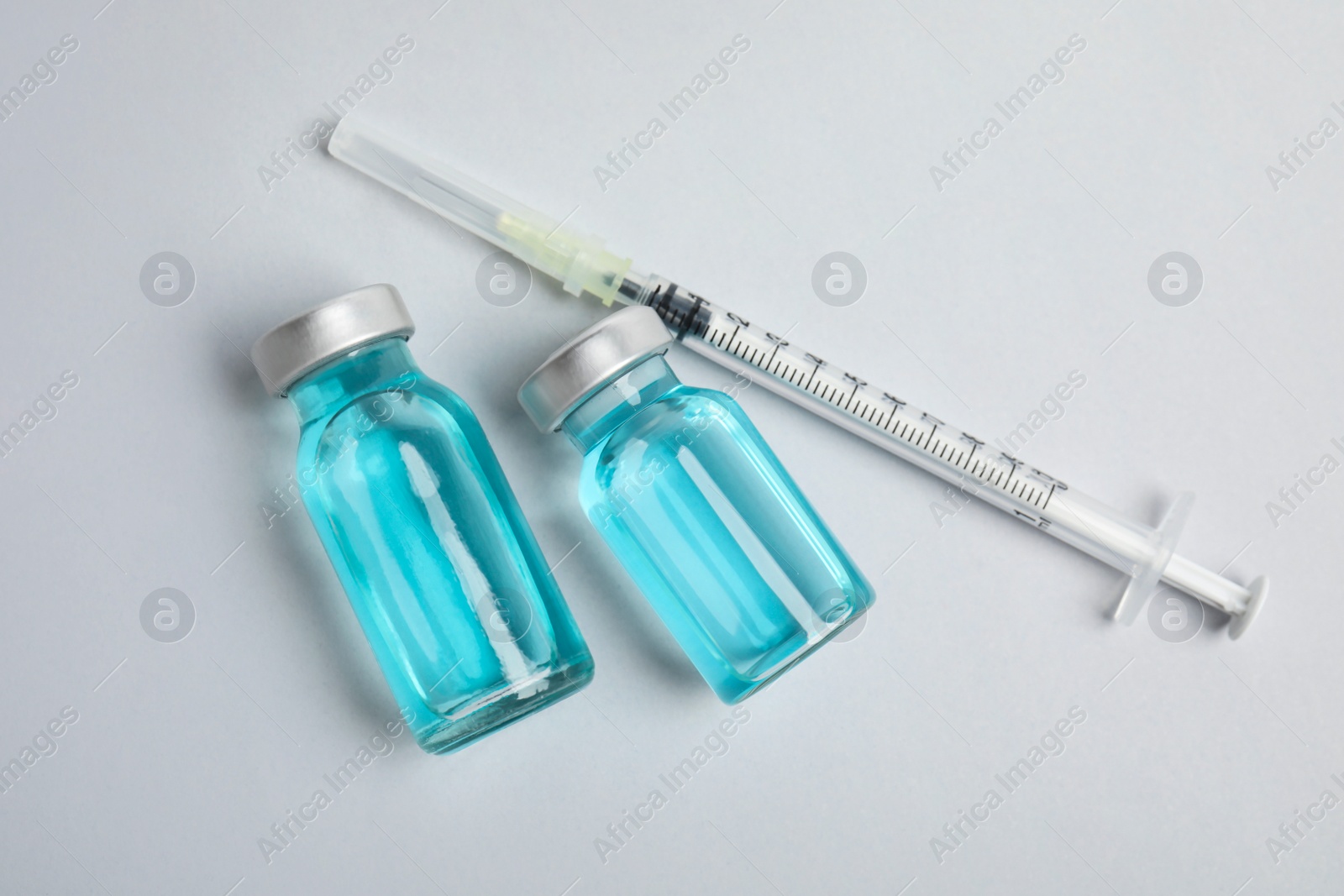 Photo of Vials and syringe on light background, flat lay. Vaccination and immunization