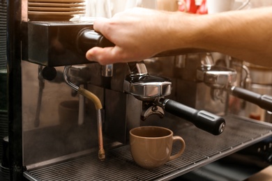 Male barista making espresso using professional coffee machine, closeup