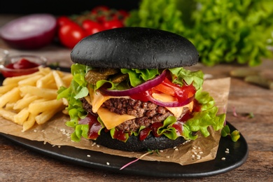 Photo of Plate with black burger and French fries on table