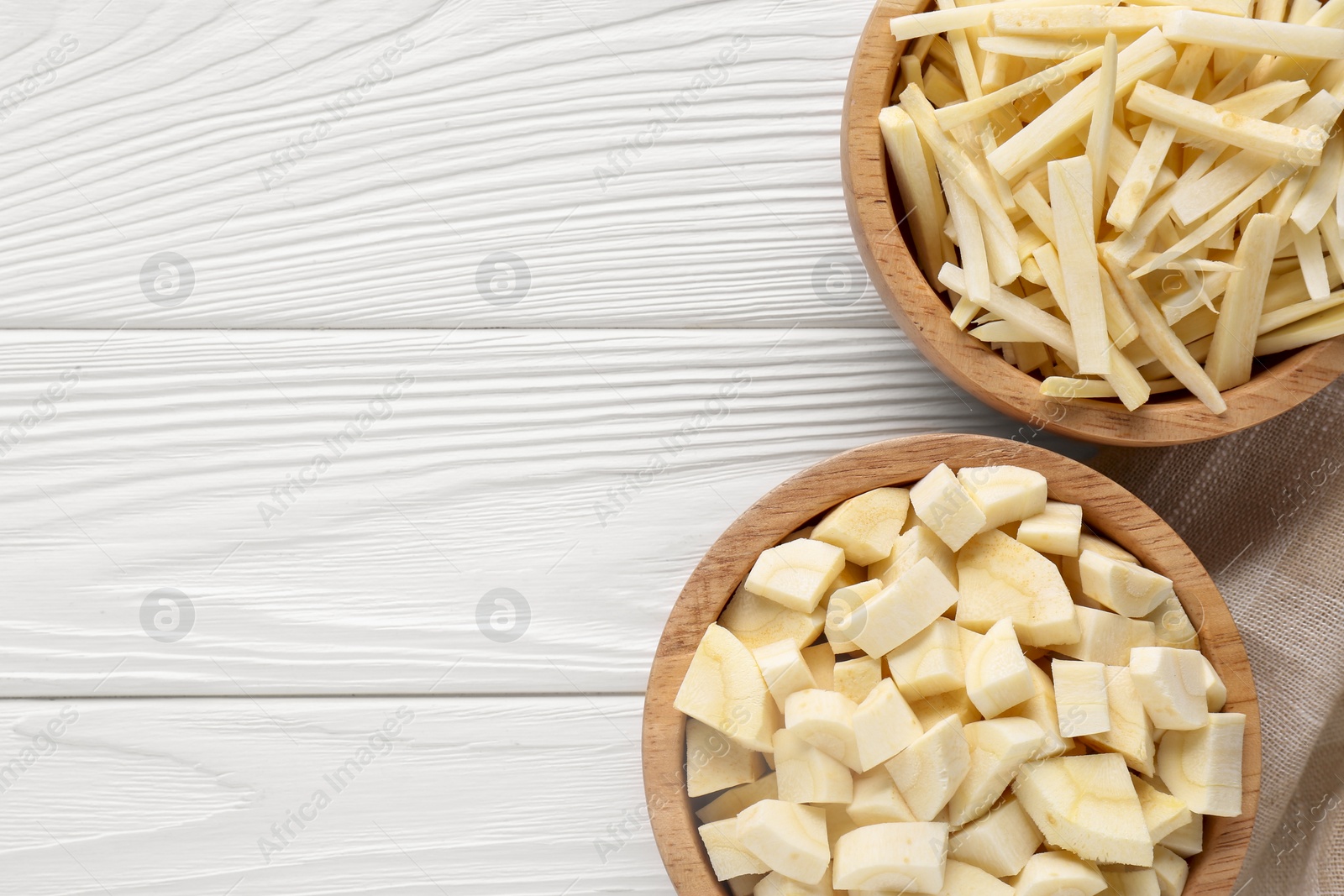 Photo of Bowls with cut parsnip on white wooden table, flat lay. Space for text