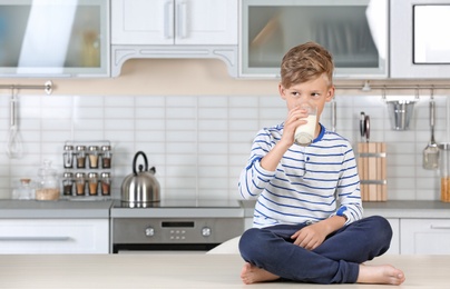 Photo of Adorable little boy with glass of milk in kitchen