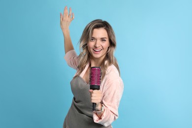 Photo of Beautiful young woman singing into hairbrush on light blue background