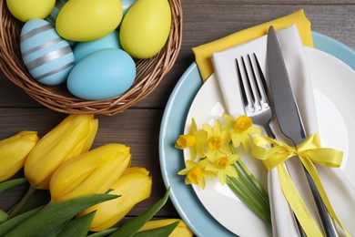 Photo of Festive table setting with flowers and painted eggs on wooden background. Easter celebration