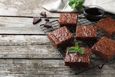 Photo of Cooling rack with delicious chocolate brownies and fresh mint on wooden table. Space for text