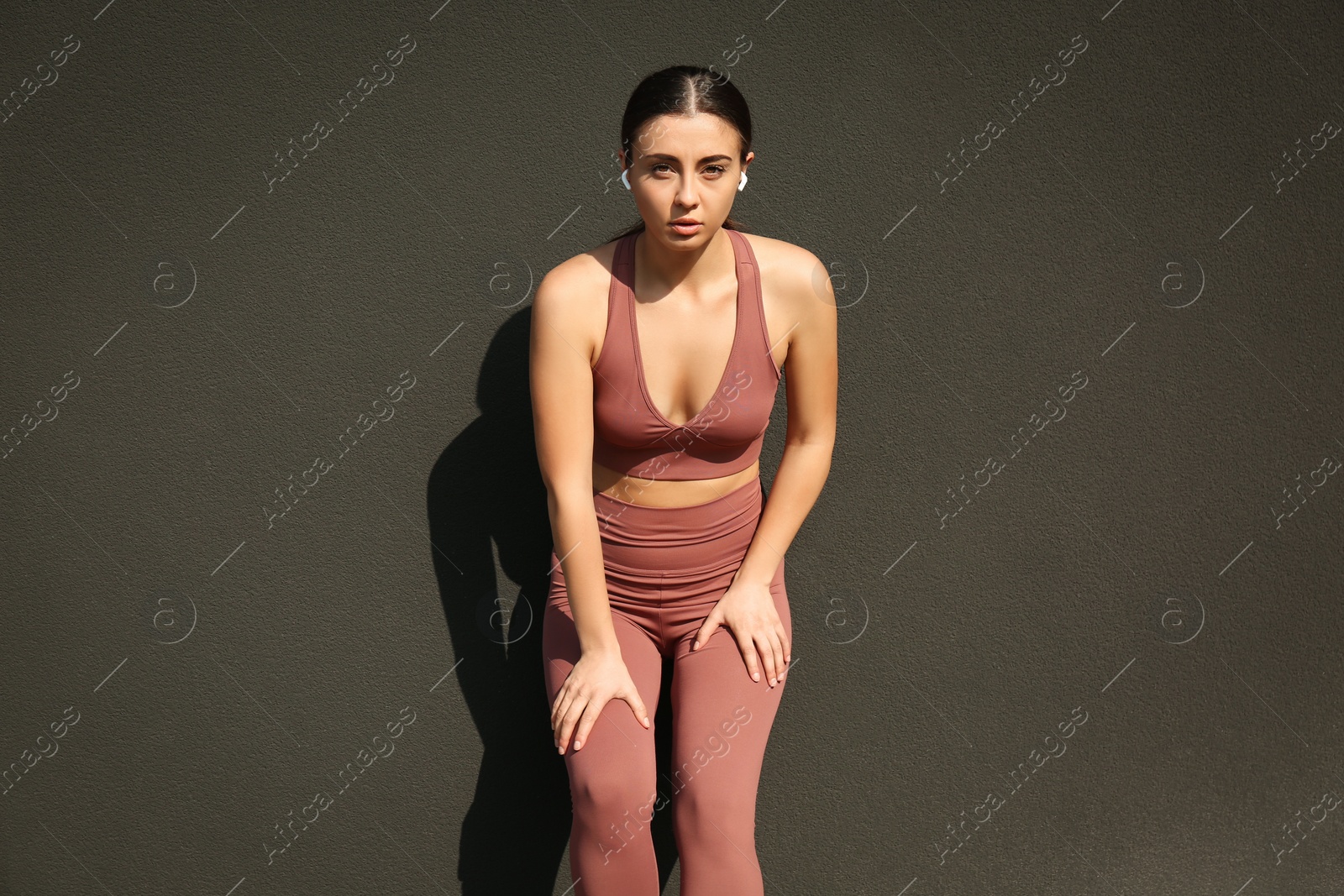 Photo of Young woman in stylish sports wear resting near grey wall