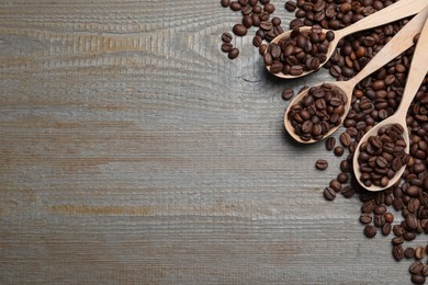 Photo of Spoons with roasted coffee beans on wooden table, flat lay. Space for text