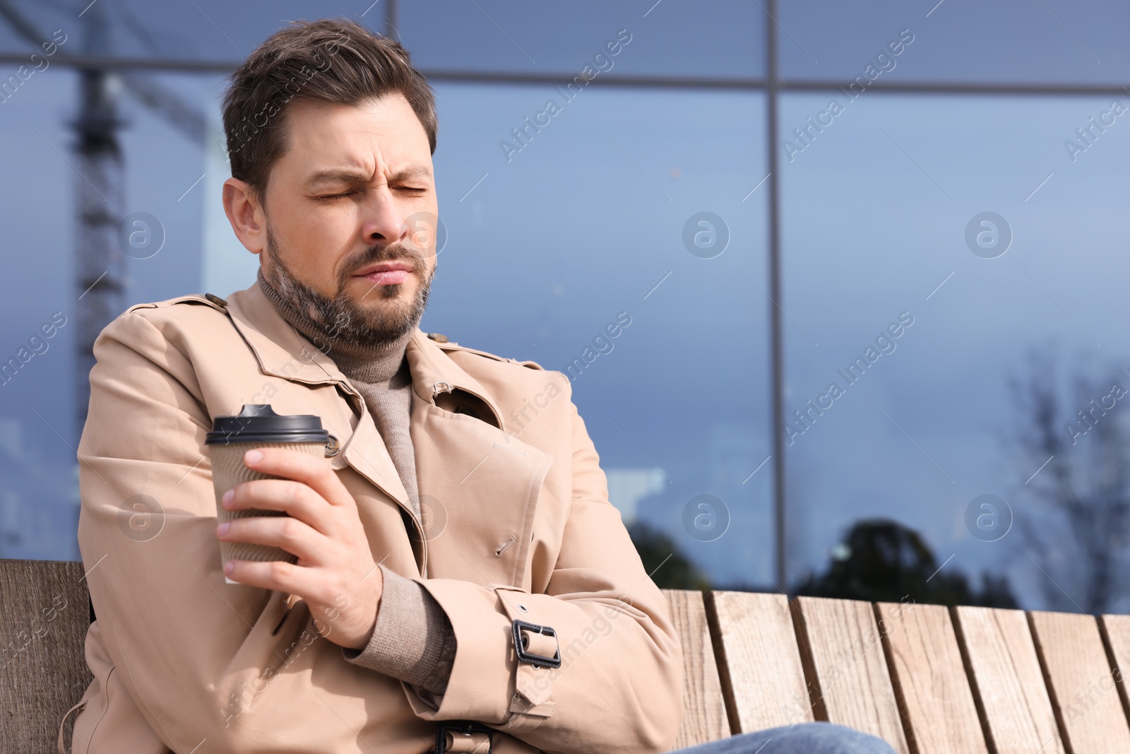 Photo of Sleepy tired man with cup of coffee on wooden bench outdoors. Space for text