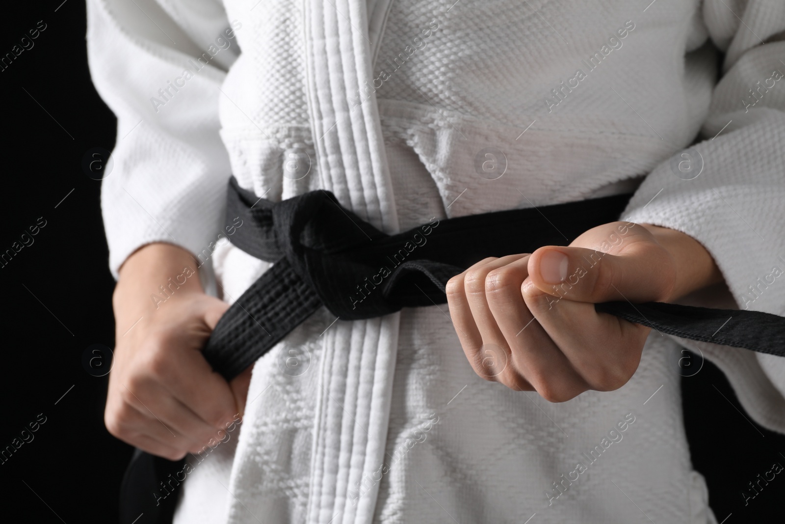 Photo of Man in keikogi with black belt on dark background, closeup. Martial arts uniform