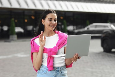 Happy young woman using laptop for video chat on city street