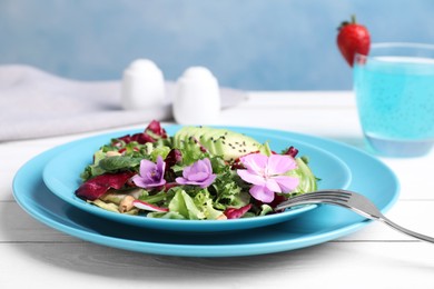 Photo of Fresh spring salad with flowers served on white wooden table, closeup