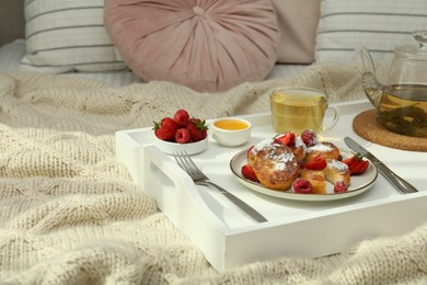 Photo of Tasty breakfast served in bedroom. Cottage cheese pancakes with fresh berries and icing sugar on wooden tray